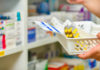 A hand holding a basket with various leaflets and boxes of pills.