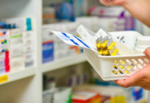 A hand holding a basket with various leaflets and boxes of pills.