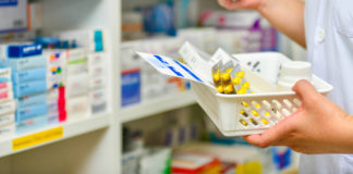 A hand holding a basket with various leaflets and boxes of pills.