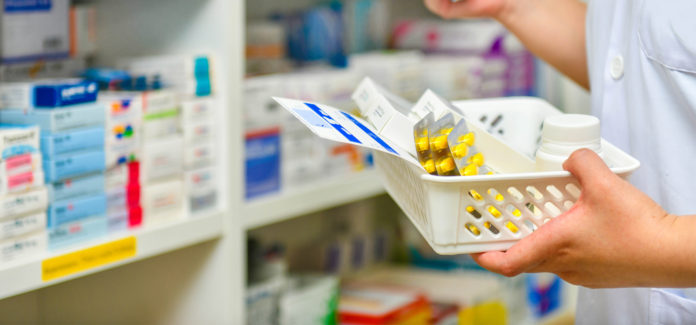 A hand holding a basket with various leaflets and boxes of pills.